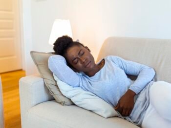 Woman lying on sofa looking sick in the living room. Beautiful young woman lying on bed and holding hands on her stomach. Woman having painful stomachache on bed, Menstrual period Managing PCOS Without Birth Control